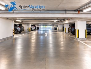 A multi-level parking garage with a clear directional arrow on the floor, multiple parking spaces, and a logo for Spice Vacation Rentals. - Beachfront 3 Bdrm Gem in Isla Verde Walk 2 Eat (Carolina)