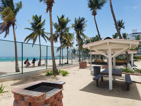 Un patio frente a la playa con una parrilla, asientos y un espacio cubierto.