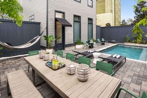 Relax by the pool in a serene outdoor space with a long table, chairs, and a hammock.