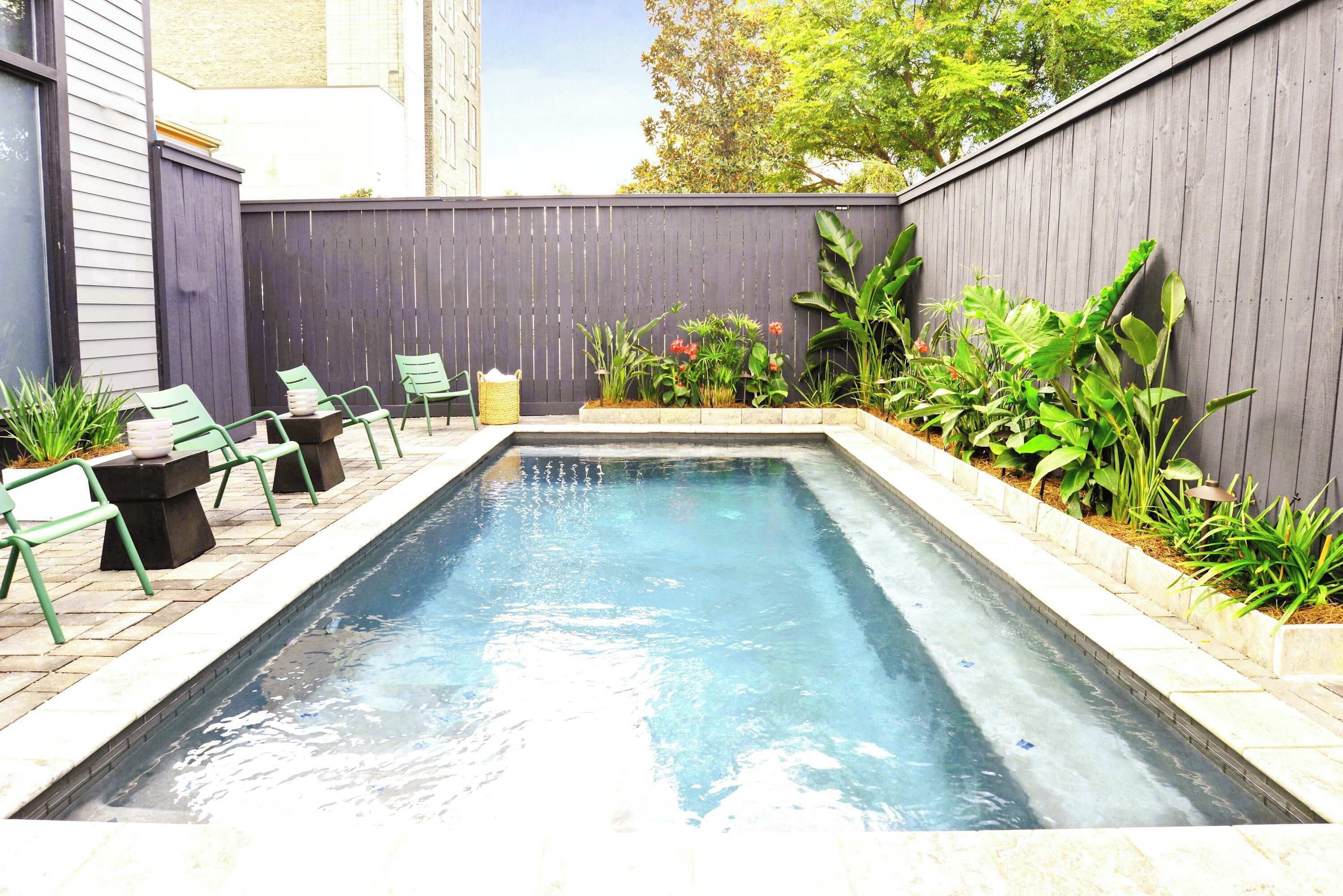 Une piscine rectangulaire dont le bord est recouvert de carreaux, entourée d’un petit muret en pierre et de différentes plantes.