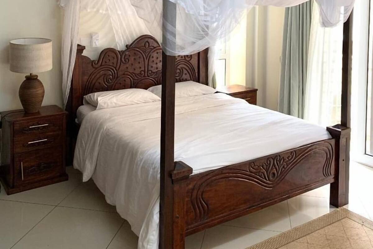 A four-poster bed with a canopy, wooden headboard, bedside tables, and a floor lamp.