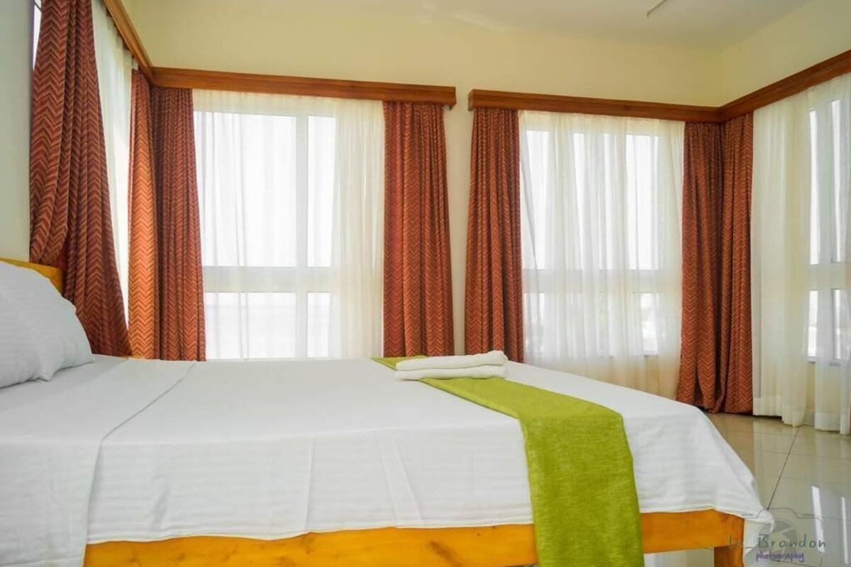 A hotel room with a large bed, two windows with curtains, and a wooden headboard.
