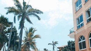 A swimming pool with clear blue water, surrounded by a white wall and a building with multiple windows. - Stay.Plus APA Apartments Nyali (Mombasa)