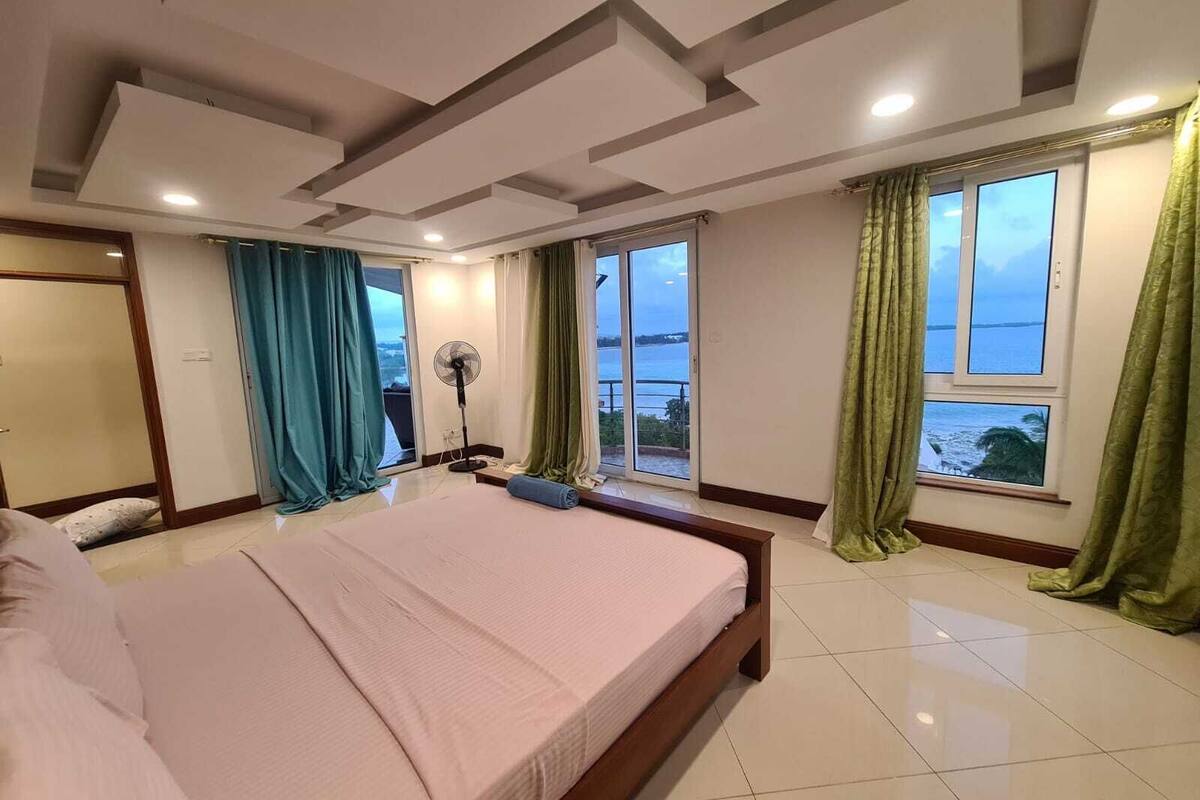 A bedroom with a large bed, a sliding glass door to a balcony, and a view of the sea.