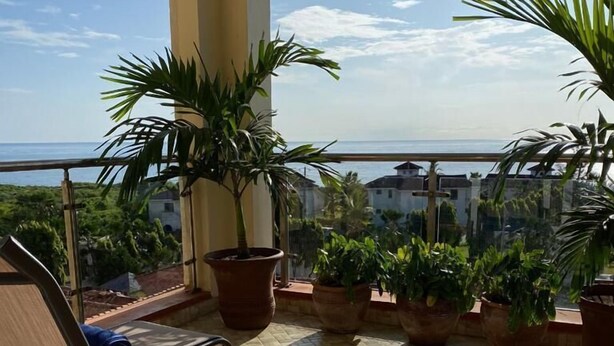 A balcony with two lounge chairs, potted plants, and a view of the sea and buildings. - Stay.Plus APA Apartments Nyali (Mombasa)