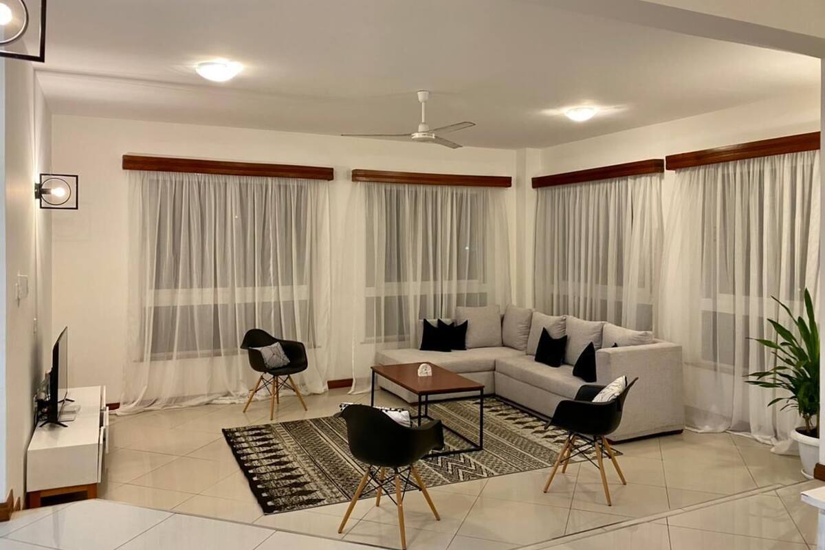 A modern living room with a sectional sofa, two black chairs, a coffee table, and a TV on a stand.