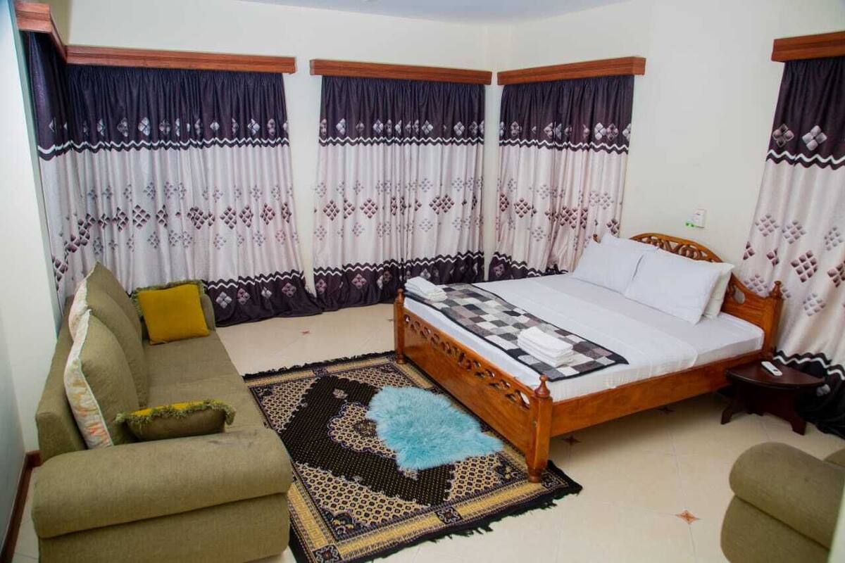 A bedroom with a wooden bed, a sofa, a patterned rug, and curtains with a diamond pattern.