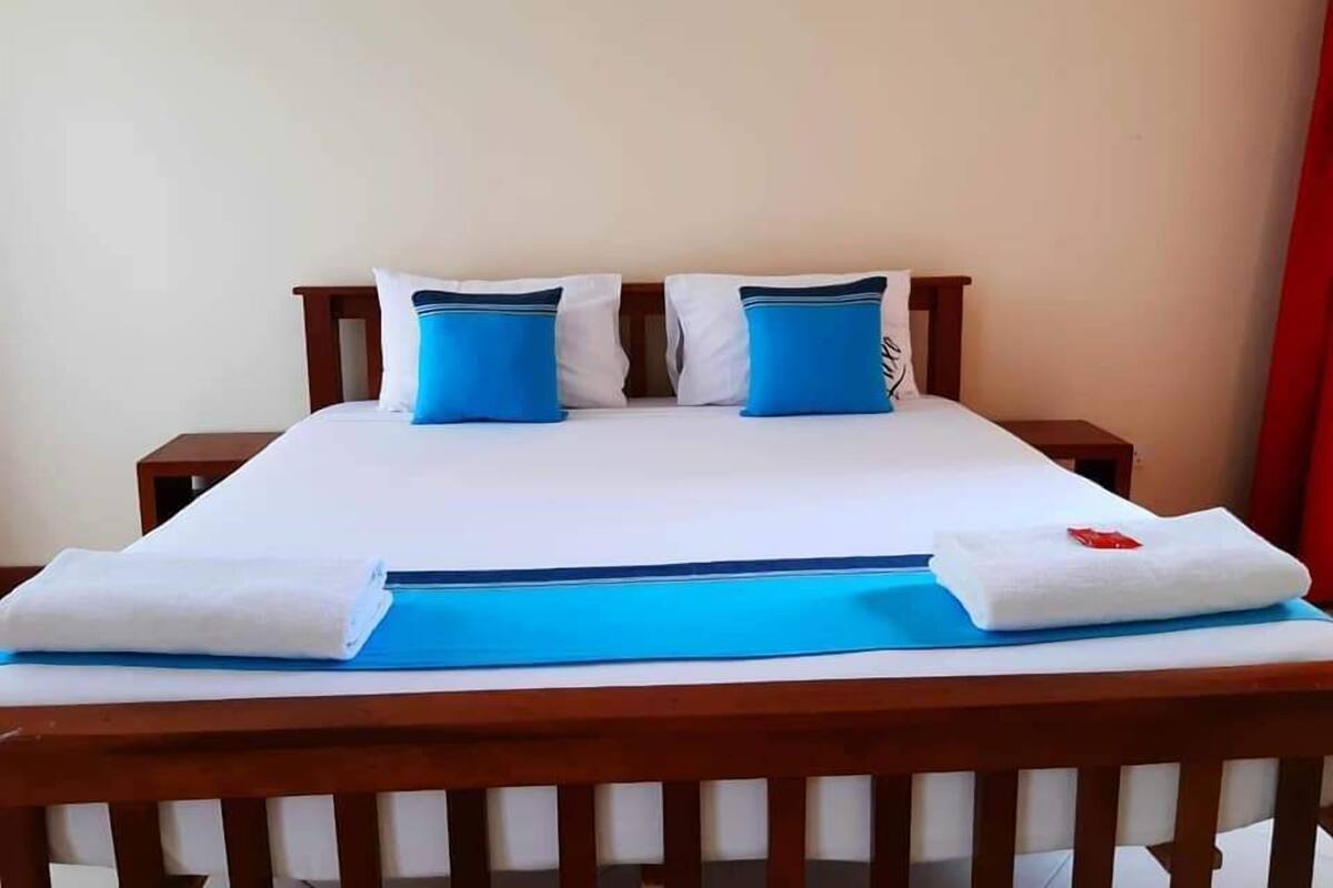 A neatly made bed with white and blue bedding, two pillows, and a blue towel on the side.