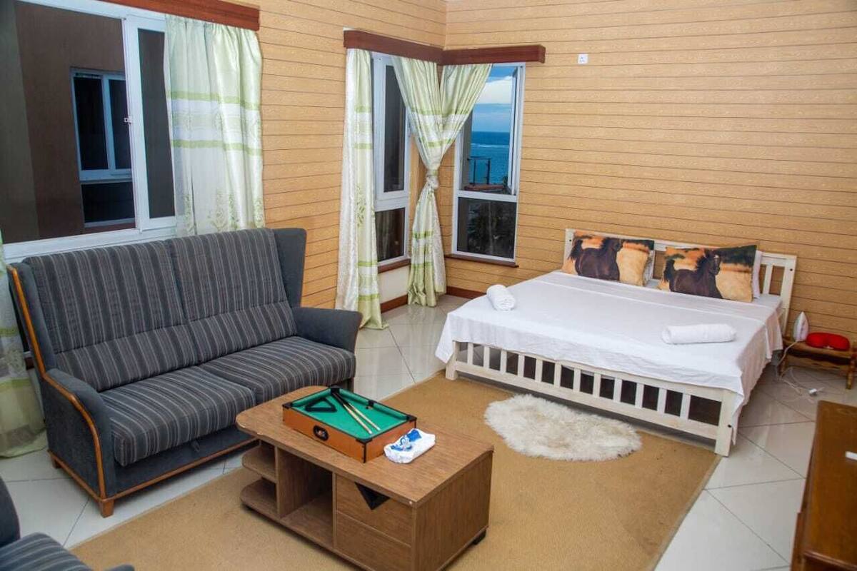 A room with a sofa, a bed, a pool table, and windows with curtains.