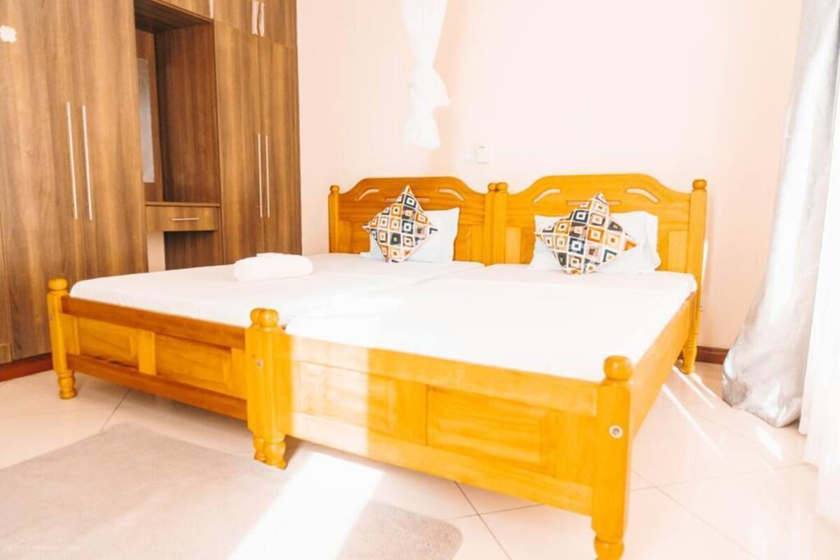 A double bed with a wooden frame and white bedding, a wooden wardrobe, and a white curtain.