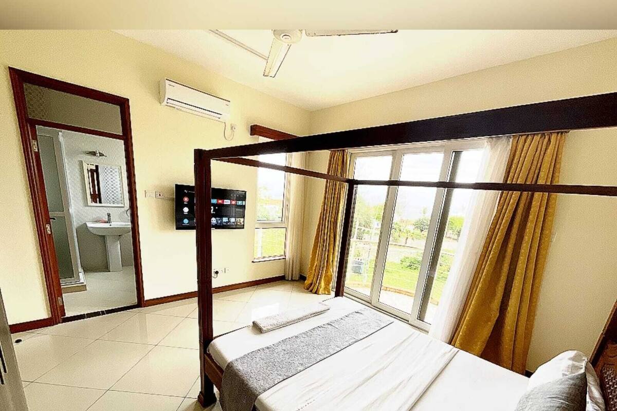 A bedroom with a four-poster bed, a television, and a bathroom visible through an open door.