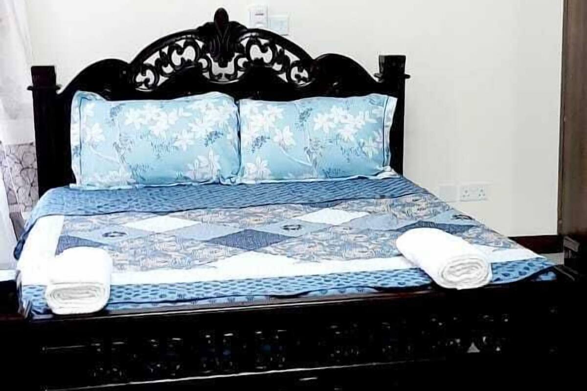 A bed with a floral-patterned bedspread and matching pillows, a dark wooden headboard, and a red rug on the floor.