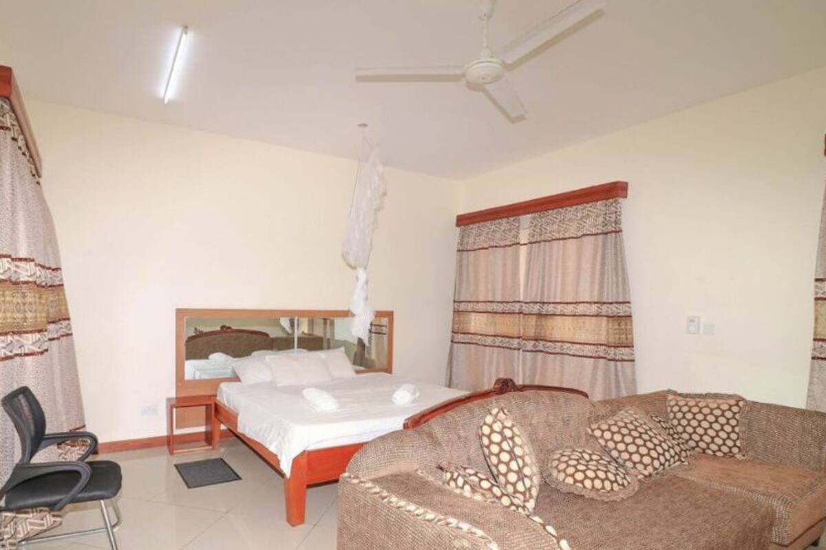 A bedroom with a bed, a sofa, a chair, and curtains.