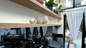 A modern kitchen with black countertops, a stainless steel sink, and wooden shelves above holding dishes and potted plants. - Design Led 1 bed in Cosmopolitan Queens Park (London)