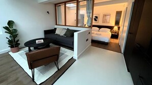 A modern, compact living space with a sofa, a small coffee table, a potted plant, and a bed in the background. - Design Led 1 bed in Cosmopolitan Queens Park (London)