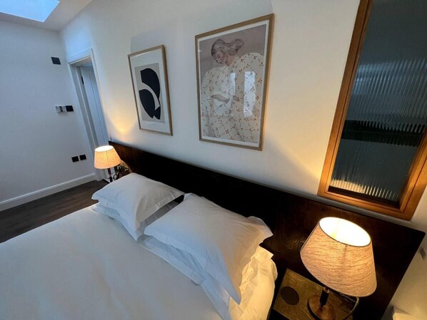 A hotel room with a large bed, two framed artworks on the wall, a bedside lamp, and a window with blinds.