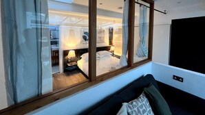 A hotel room with a large window, a bed, a desk with a lamp, and a television. - Design Led 1 bed in Cosmopolitan Queens Park (London)