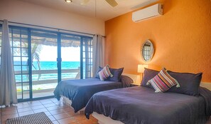 Una camera d'albergo con due letti, un'ampia finestra vista mare, un condizionatore d'aria e un piccolo specchio a parete.