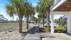 A wooden pathway lined with palm trees leading to a building with a covered porch. - Single Family Barrier Dunes, Pool ~ BD 108-207 (Cape San Blas)