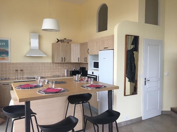 Une cuisine avec une table en bois dressée pour quatre personnes, un réfrigérateur blanc et des placards de couleur claire.