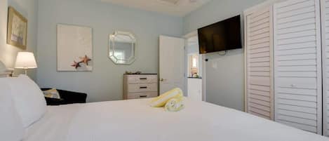 Habitación de hotel con cama, televisión montada en la pared, espejo y armario.