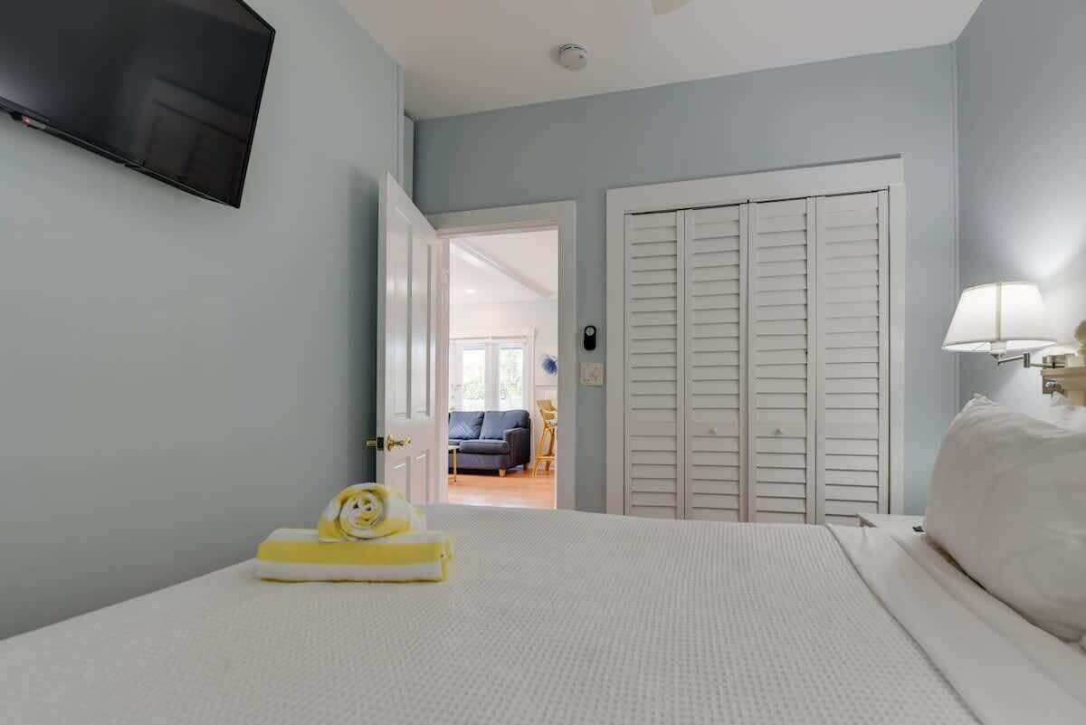 A bedroom with a bed, a TV mounted on the wall, and a door leading to another room.