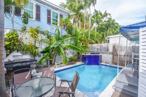 A backyard with a swimming pool, a barbecue grill, and a dining area with chairs and a table. - Poolside Suite - Pool & Close to Duval Street (Key West)