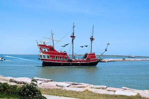 A large, red and black fishing boat docked at a rocky shore with clear blue water and a distant shoreline.