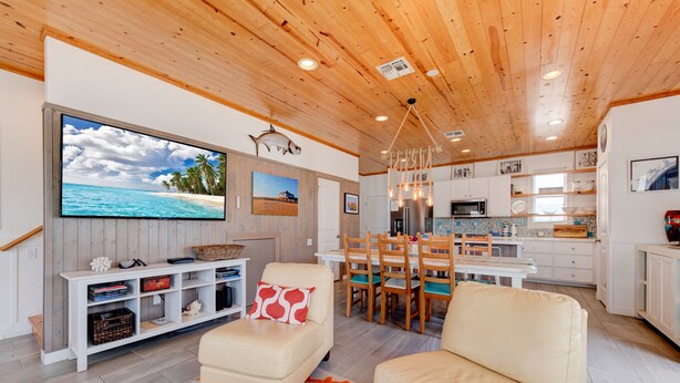 A modern living room with a TV, comfortable seating, a wooden ceiling, and a kitchen area with white cabinets and a dining table. - Gorgeous, pet friendly, coastal cottage within walking distance to the restauran (Port Aransas)