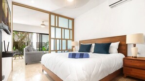 Ein modernes Schlafzimmer mit einem großen Bett, einem Holzkopfende, zwei Nachttischlampen und Blick auf einen Balkon mit Pflanzen.