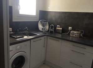 Cozinha compacta com máquina de lavar, cafeteira, rádio e janela que proporciona iluminação natural.