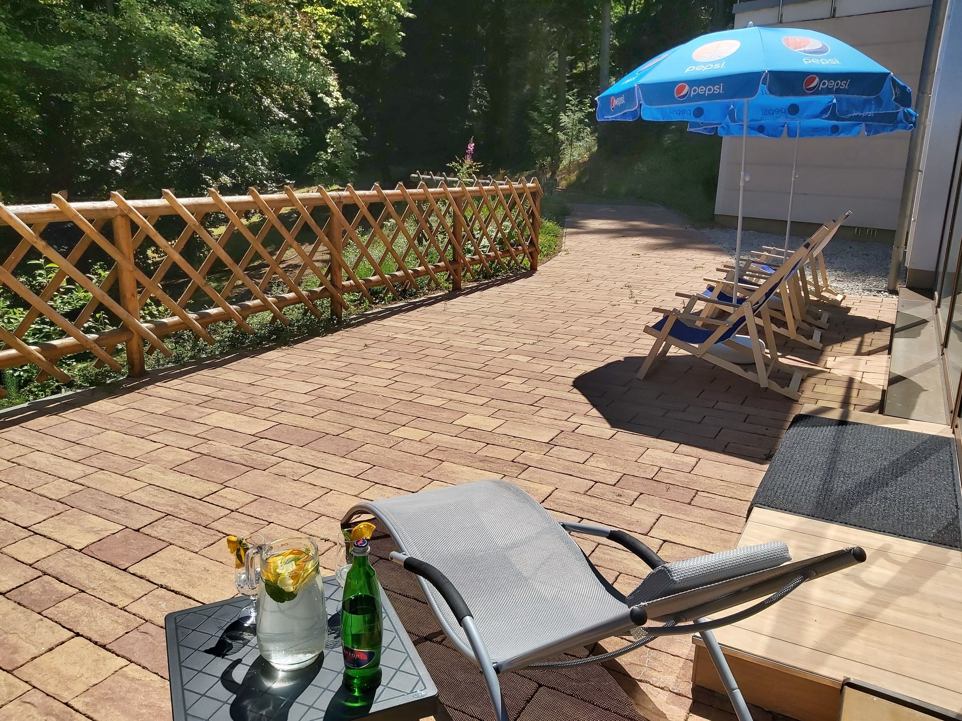 Un patio al aire libre con una mesa, sillas, un paraguas de Pepsi y una valla de madera.