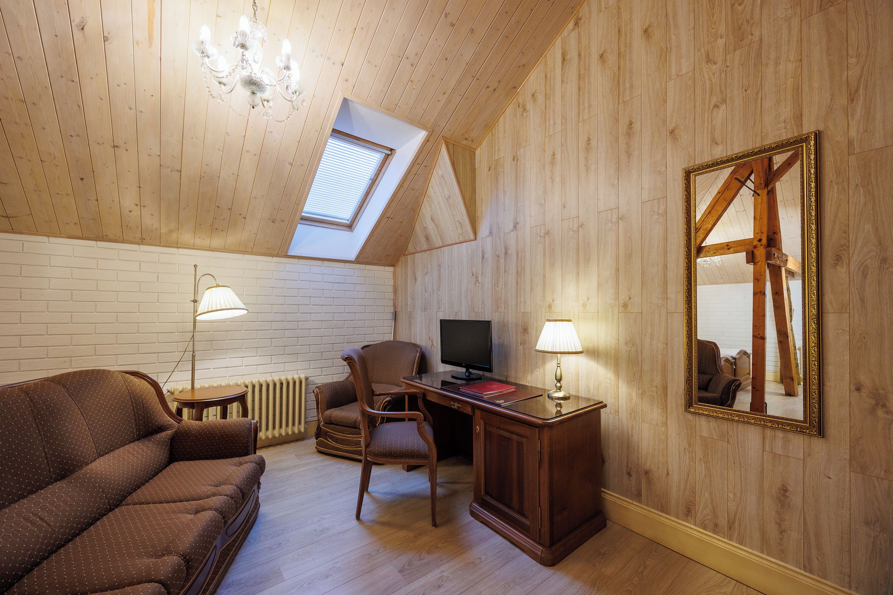 Un dormitorio tipo loft con techo inclinado, paredes de madera, un sofá, un escritorio, una silla, un televisor y un espejo grande.