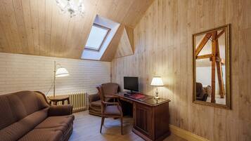Un dormitorio tipo loft con techo inclinado, paredes de madera, un sofá, un escritorio, una silla, un televisor y un espejo grande.