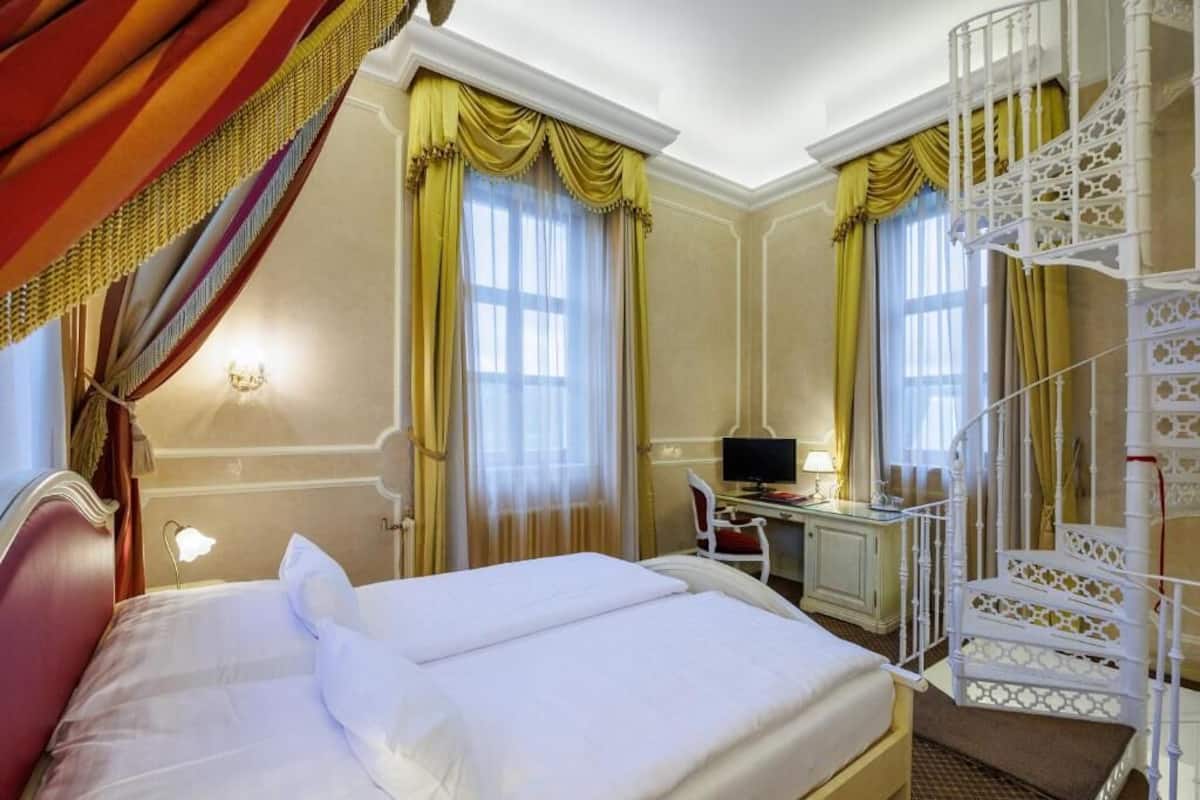 A hotel room with a bed, a desk, a computer, and a staircase.