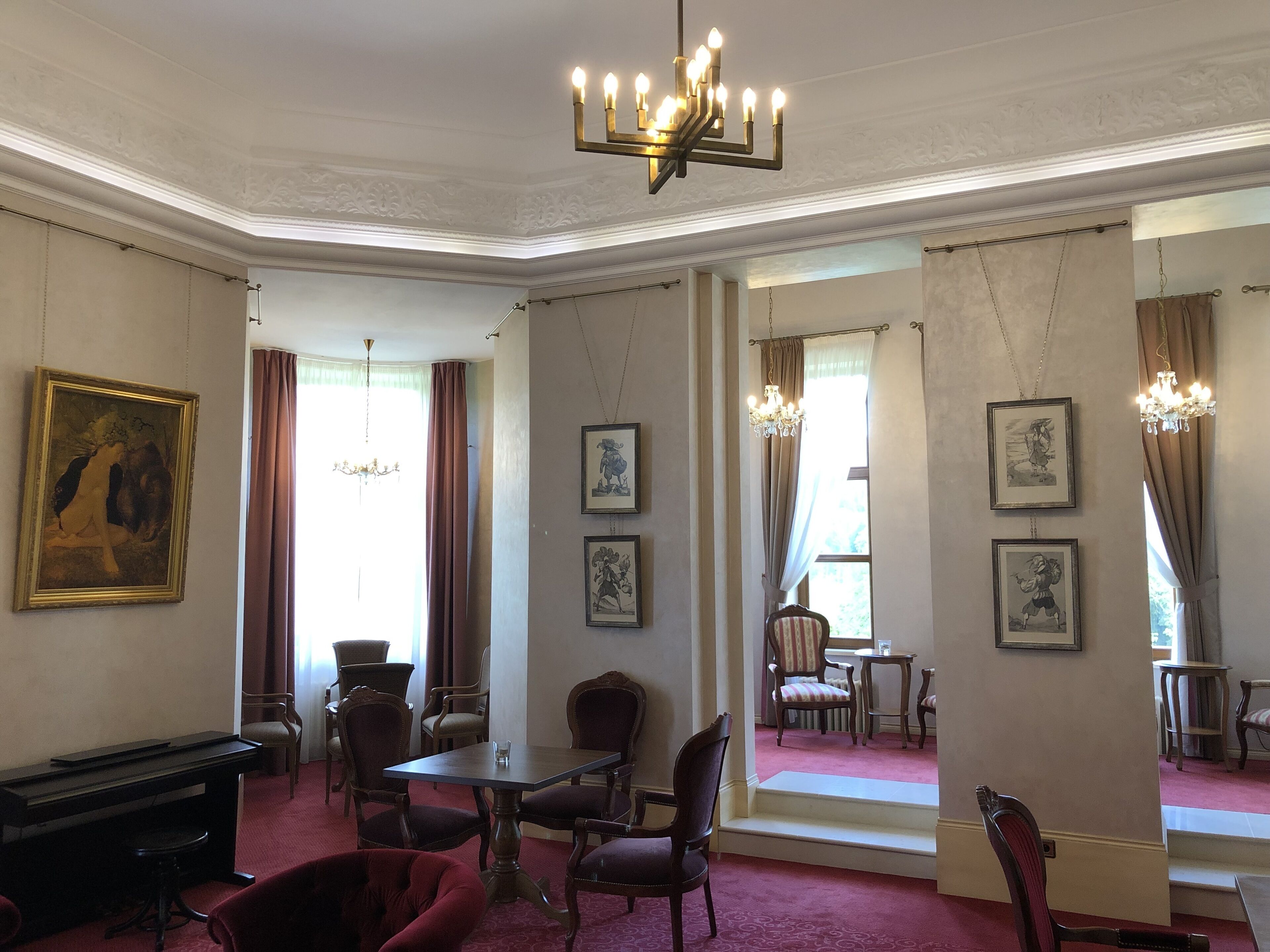 A room with a piano, a dining table with chairs, a chandelier, and framed pictures on the walls.