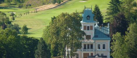 A large building with a tower, surrounded by a golf course and trees.