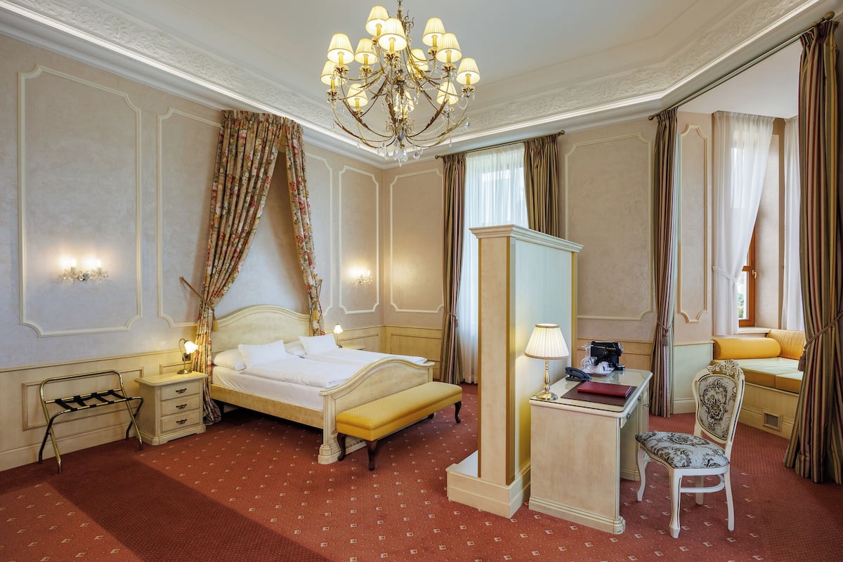 A hotel room with a bed, bedside table, lamp, chair, and a desk with a mirror.