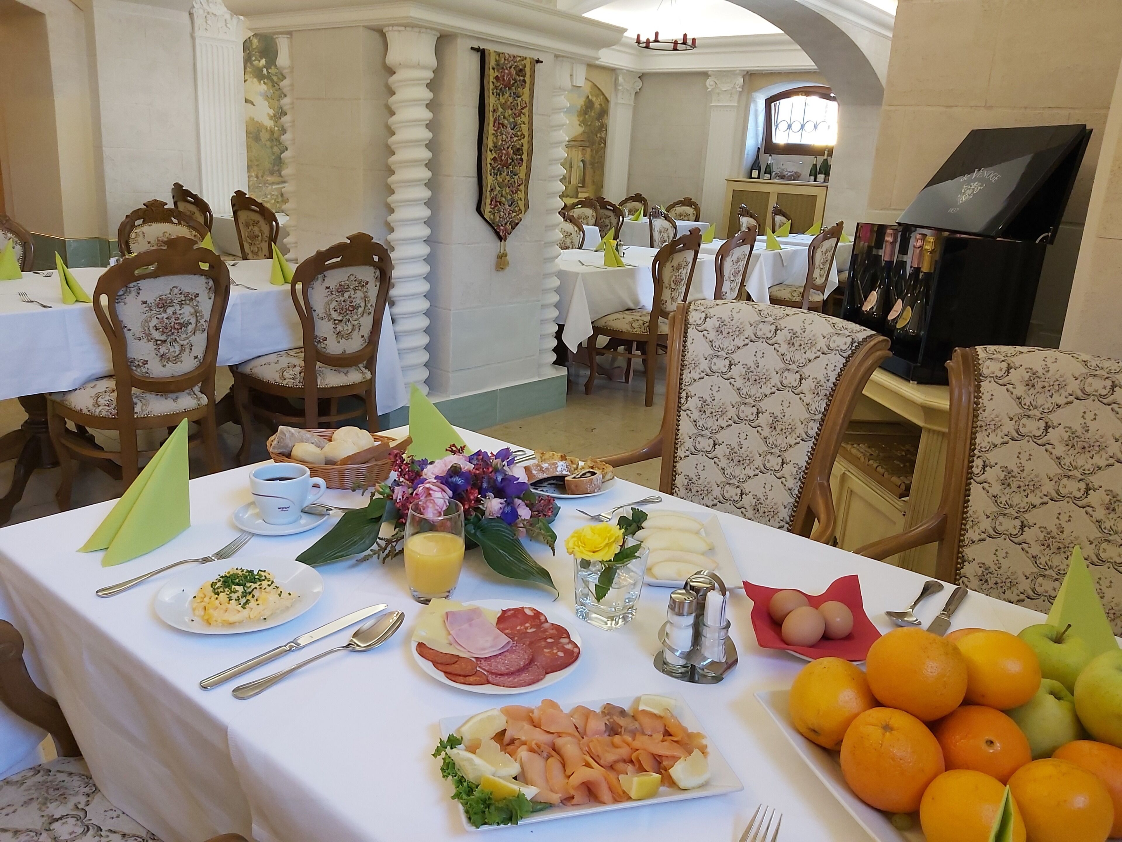Comedor con varias mesas dispuestas para el desayuno, que ofrece una variedad de platos, frutas y bebidas.