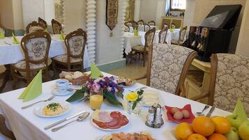 Comedor con varias mesas dispuestas para el desayuno, que ofrece una variedad de platos, frutas y bebidas.