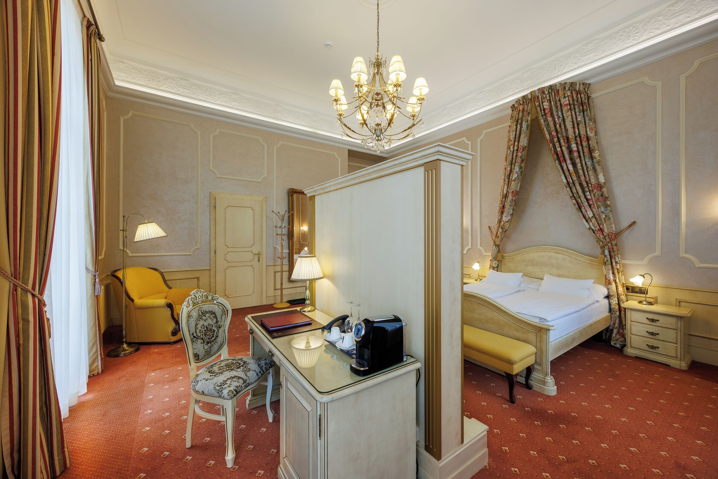 Una habitación de hotel con cama, escritorio, silla, mesita de noche, lámpara y espejo.