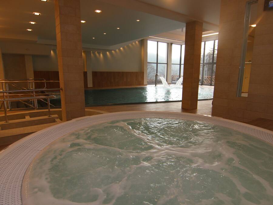 Een bubbelbad in een goed verlichte binnenzone, met uitzicht op een zwembad daarbuiten.