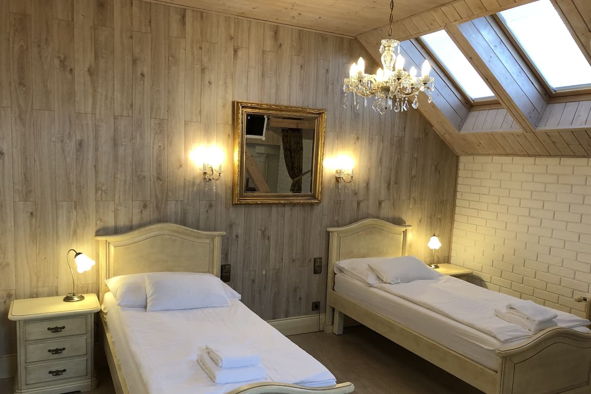 A bedroom with two beds, wooden walls, a skylight, and a chandelier.