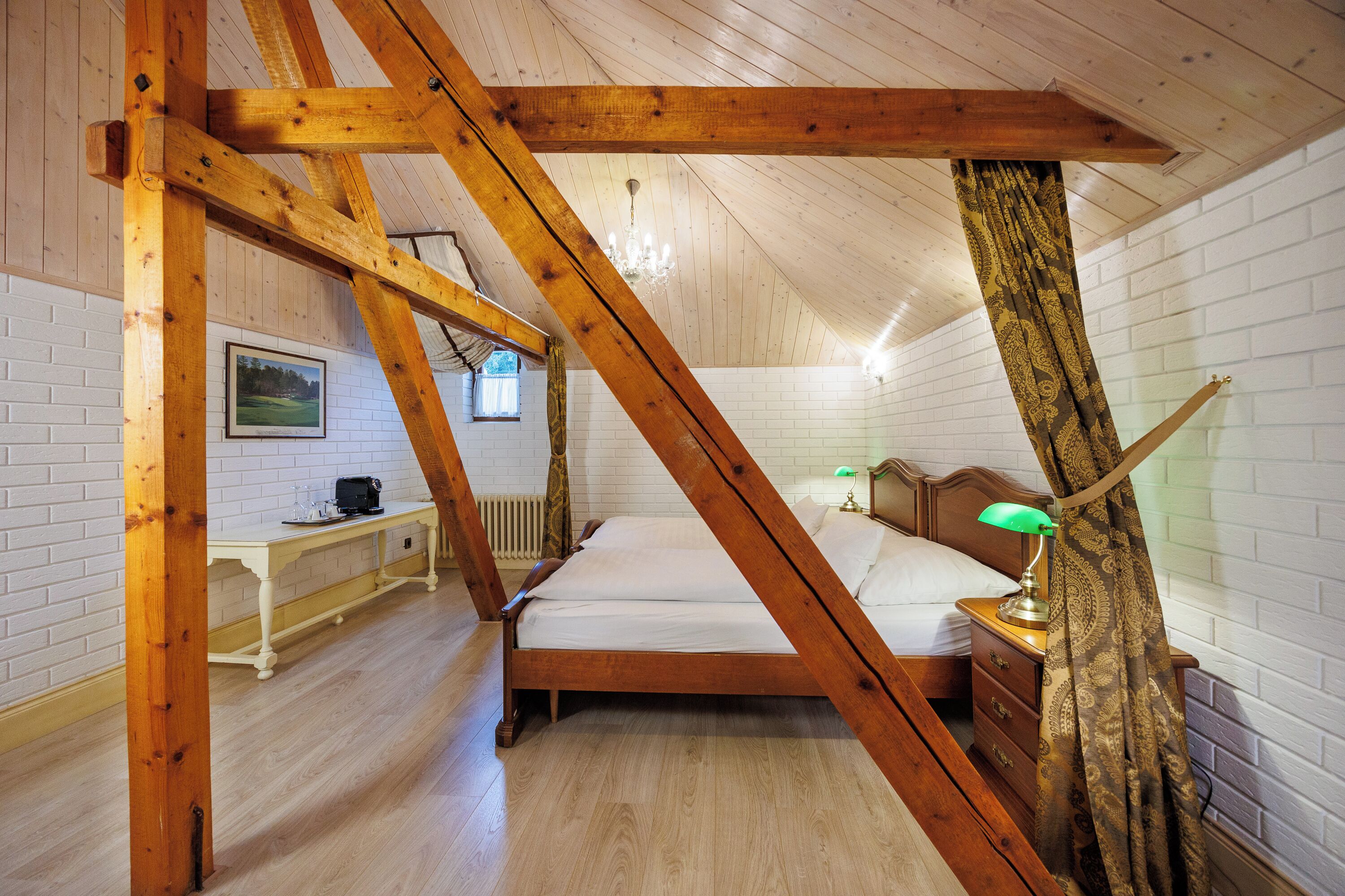 A bedroom with a wooden ceiling, a bed, a bedside table with a lamp, and a desk with a chair.
