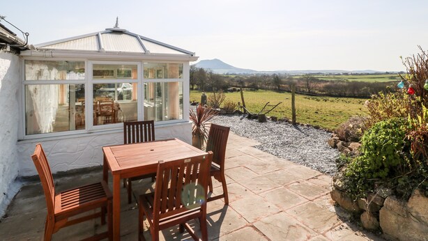 A conservatory with a table and chairs, overlooking a rural landscape with a mountain in the distance. - Y Big (Pwllheli)