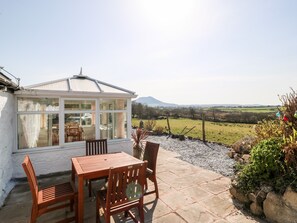 Ein Wintergarten mit Tisch und Stühlen, der auf eine ländliche Gegend mit einem Berg in der Ferne blickt.