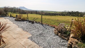 A stone pathway leading to a grassy field with a mountain in the background. - Y Big (Pwllheli)