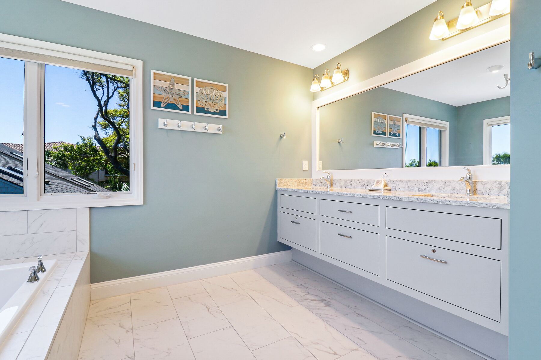 Une salle de bain moderne dotée d’un grand miroir, d’une baignoire et d’un meuble-lavabo avec plusieurs tiroirs.
