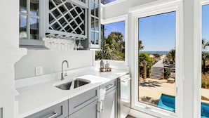 A modern kitchen with a large window, a built-in wine rack, and a view of a pool and beach.