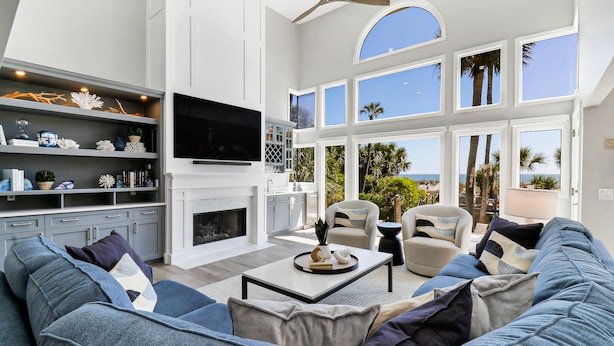 A spacious living room with a fireplace, a large TV, and a view of the beach.